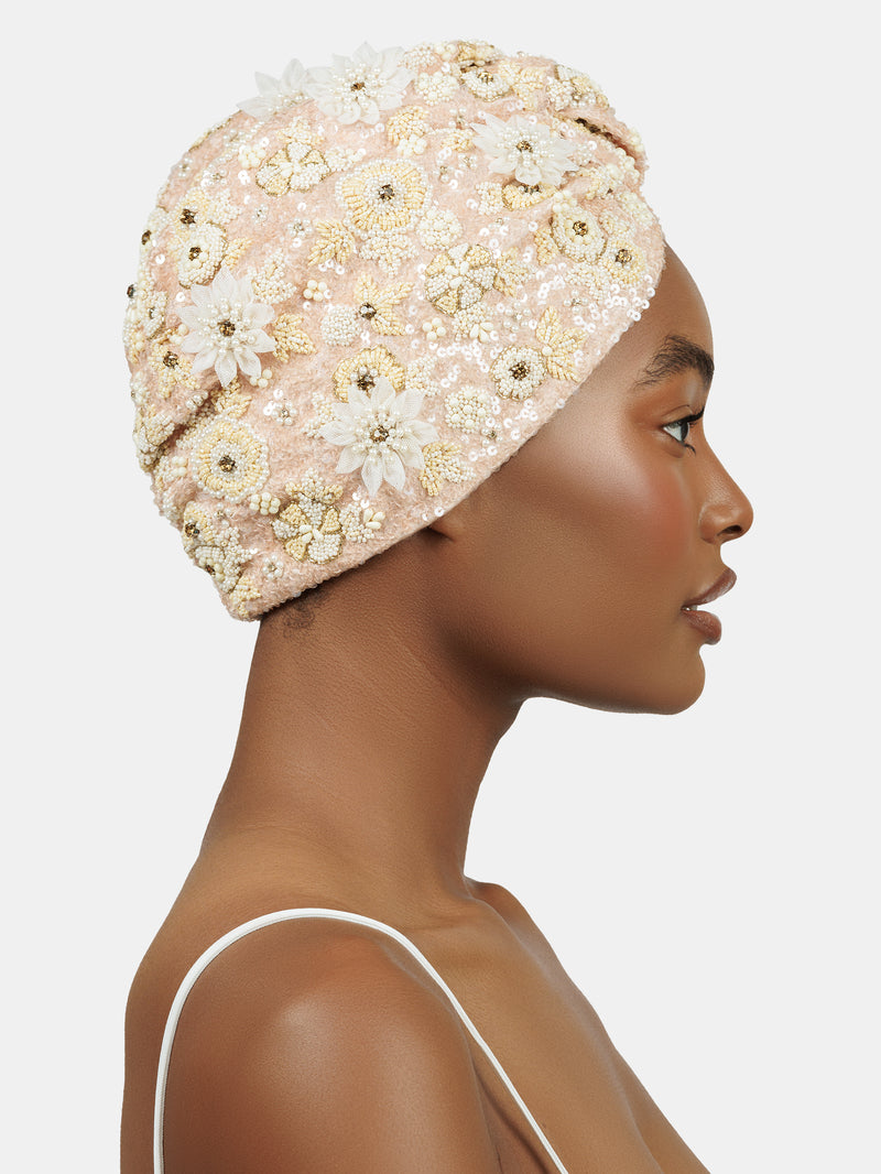 Profile view of black female model wearing  hand made sequin-embellished peach color turban with a tridimensional tonal flower pattern design by Maryjane Claverol