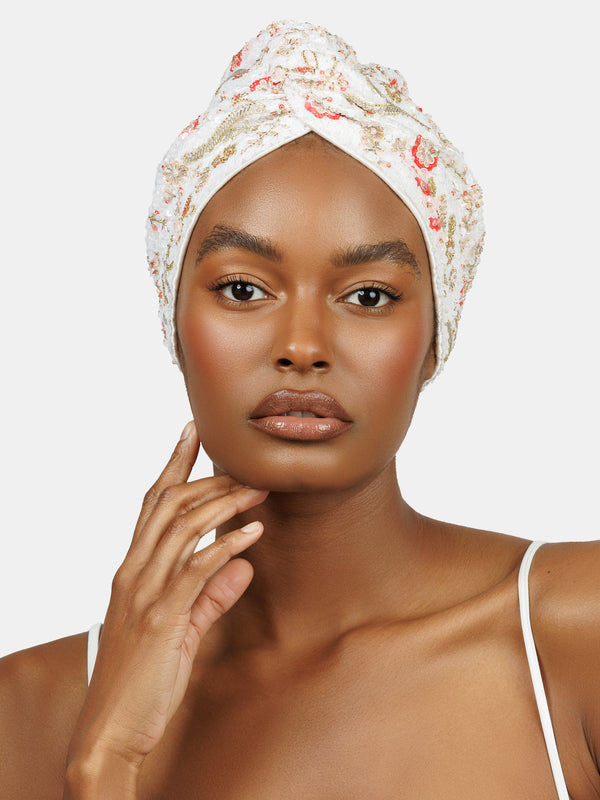 Black female model wearing hand made sequin-embellished white turban with a delicate red and pink flower pattern designed by Maryjane Claverol
