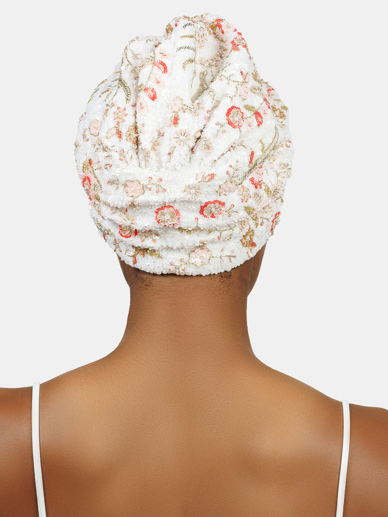 Back view of black female model wearing hand made sequin-embellished white turban with a delicate red and pink flower pattern designed by Maryjane Claverol
