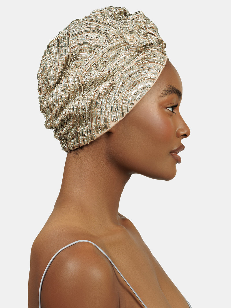 Side view of female model wearing handmade silver sequin and palette embroidered blush colored turban designed by Maryjane Claverol